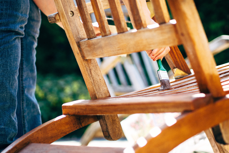 Teakmöbel müssen im Gegensatz zu vielen anderen Gartenmöbeln nicht geölt werden Eine Person ölt einen Teak-Stuhl