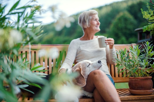 Ältere Dame sitzt mit Hund auf Bank im Garten