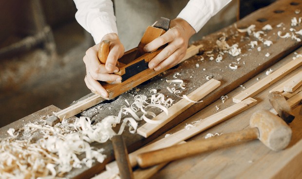 Ein Tischler hobelt an einem Holzstück, das für ein Möbelstück bestimmt ist