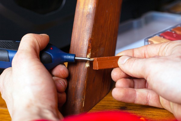 Eine schadhafte Stelle an einem hölzernen Tischbein wird mit speziellem Wachs ausgebessert Holzschäden ausbessern