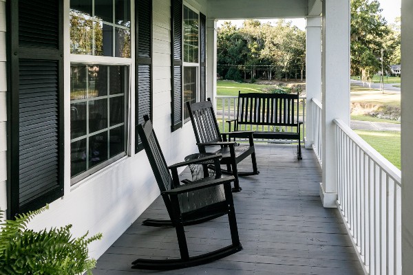 Auf einer schmalen Veranda stehen Schaukelstühle und eine Bank Veranda im Landhausstil