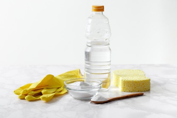 Essig ist ein effektives Mittel, um Rauchgeruch aus Möbeln zu entfernen Eine Flasche Essig, ein Schwamm und Plastikhandschuhe warten auf den Einsatz