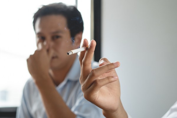 Ein Mann hält sich angeekelt die Nase zu, da im Vordergrund eine andere Person raucht Rauchgeruch