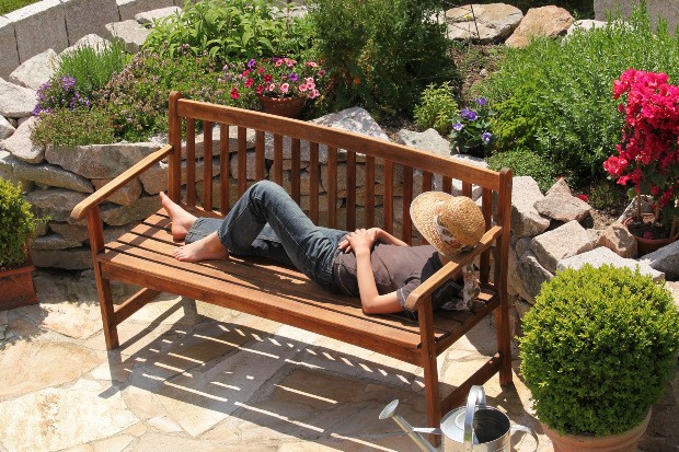 Ein Mann döst in der Sonne auf einer Gartenbank aus Holz